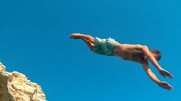 CLOSE UP: Athletic tourist jumps off a cliff to dive into the refreshing ocean. — Fotografia de Stock