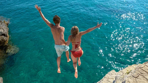 Alegre pareja de turistas decide saltar de un acantilado rocoso y sumergirse en el mar. — Foto de Stock