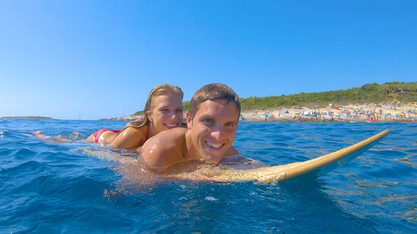PORTRAIT: Pareja turística disfruta tumbada en una tabla de surf y remando alrededor del mar —  Fotos de Stock