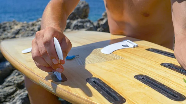 FECHAR UP: Surfista irreconhecível anexando barbatanas brancas na parte inferior de sua prancha de surf. — Fotografia de Stock