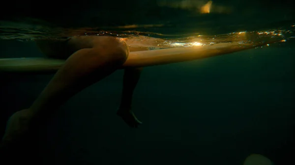 НЕОБХОДИМОСТЬ: Золотой закат светит неузнаваемой женщине, сидящей на доске для серфинга — стоковое фото