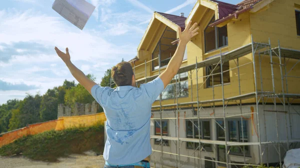 Κοντινό πλάνο: Ευτυχής αρχιτέκτονας ρίχνει τα σχέδιά του στον αέρα αφού δει ημιτελές σπίτι. — Φωτογραφία Αρχείου