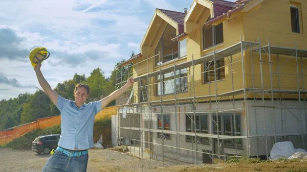 Περήφανος εργολάβος σηκώνει το καπέλο του στον αέρα μπροστά από το νέο σπίτι. — Φωτογραφία Αρχείου
