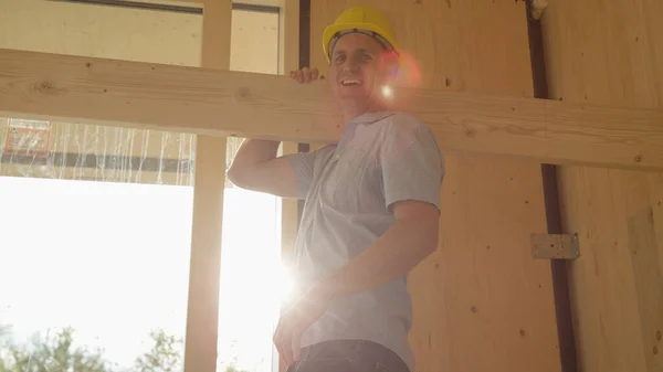 PORTRAIT: Fröhlicher Arbeiter lächelt in die Kamera, während er eine Planke durch den Raum trägt — Stockfoto