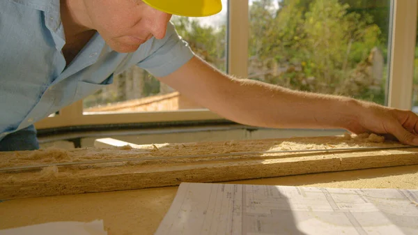 Κοντινό πλάνο: Ο ξυλουργός επιθεωρεί προσεκτικά μια σανίδα κόντρα πλακέ και τη συγκρίνει με τα σχέδια — Φωτογραφία Αρχείου
