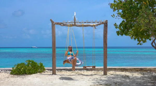 CHIUDI: Gioiosa donna dondola sulle altalene panoramiche su una spiaggia di sabbia tropicale — Foto Stock