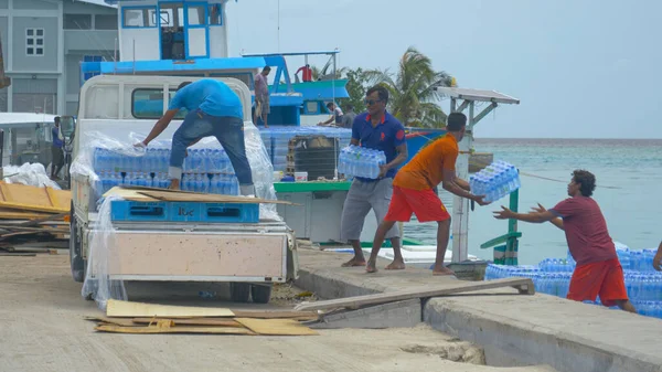 I locali collaborano per scaricare un camion e caricare una barca da carico con acqua in bottiglia — Foto Stock