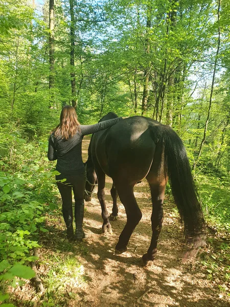 Nerozpoznatelná mladá žena kráčí lesní stezkou se svým koněm. — Stock fotografie