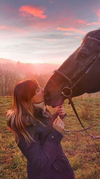 FECHAR UP: Jovem alegre beija seu cavalo no focinho ao pôr-do-sol dourado. — Fotografia de Stock