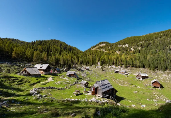 AERIAL: Lovely wooden cottages stand near forest covered mountain in Julian Alps — 图库照片