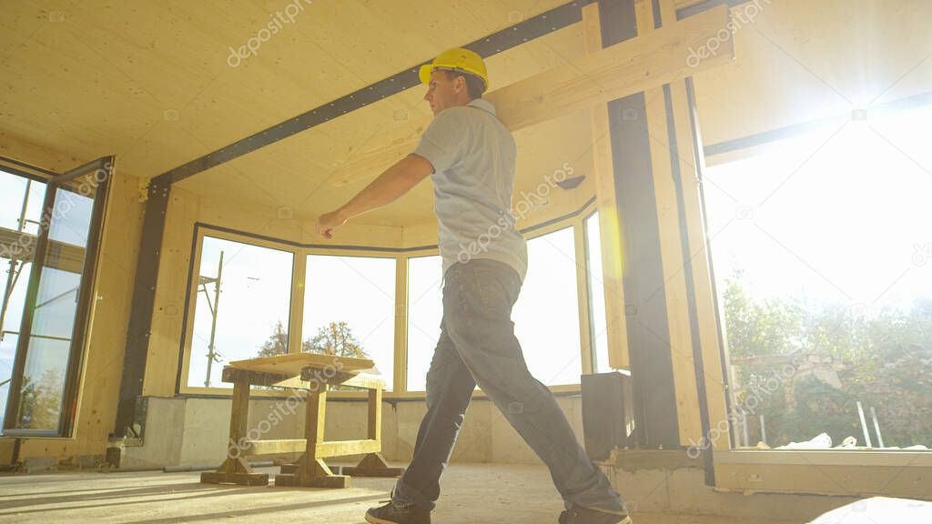 LOW ANGLE: Construction site supervisor carries a log across prefabricated house