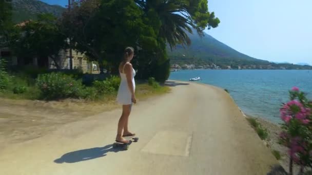 Young woman rides an electric longboard along a scenic coastal road in Croatia. — Stock Video