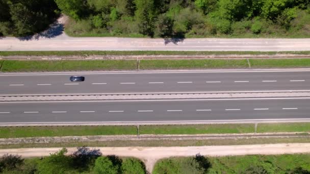 ARRIBA: Volando a lo largo de una autopista mientras los autos van y vienen a través de un bosque. — Vídeos de Stock