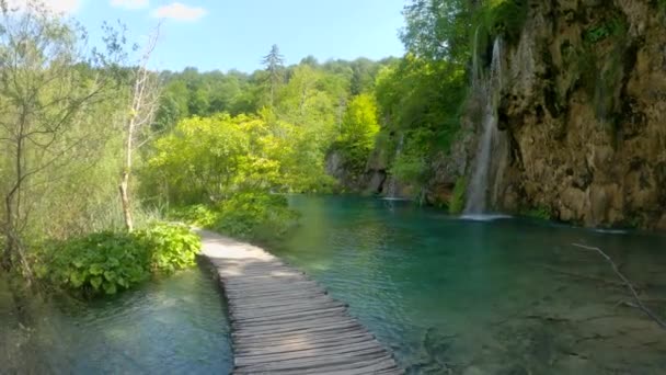 POV: Lege promenade biedt uitzicht op de waterval die uitmondt in het smaragdgroene meer. — Stockvideo