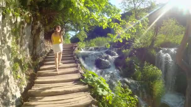 LENS FLARE: Una viaggiatrice cammina lungo una passerella che corre accanto al lago di smeraldo — Video Stock