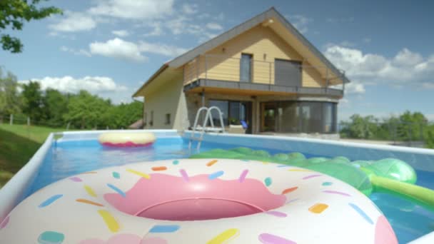 CLOSE UP: Färgglada uppblåsbara leksaker flyter runt tom trädgård pool på bakgården. — Stockvideo