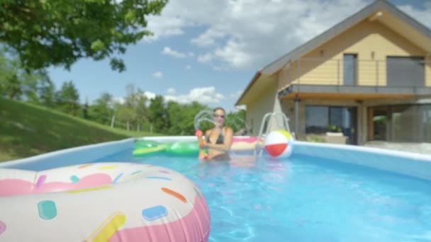 Sluiten omhoog: Gelukkig vrouw spuit water met waterpistool tijdens het spelen in huis zwembad. — Stockvideo