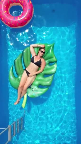VERTICAL: Young Caucasian woman lies on a big leaf floatie in her home pool. — Stock Video