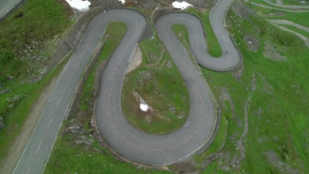 AERIAL:スイスの山の中でスイッチバック道路を自転車に乗るアクティブな観光客. — ストック動画
