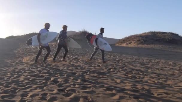Surfers running on sand to ocean — Stock Video