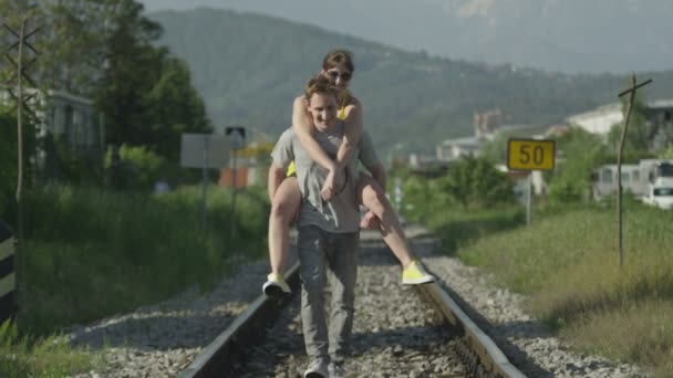 Мужчина катает свою подружку по железной дороге — стоковое видео