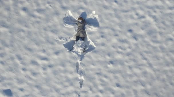 Vrouw springt in de verse sneeuw en maakt een engel — Stockvideo