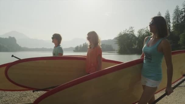 SLOW MOTION: Cheerful surfer girls carrying SUP boards to the lake at sunrise — Stock Video