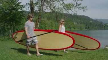 Young couple going SUPing with stand up paddle boards on lake in sunny summer