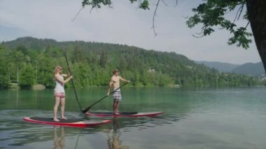 yavaş hareket yakın çekim: genç sörfçü çift göl arazi (part1 boyunca Suping)