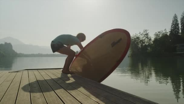 MOCIÓN LENTA: Hembra colocando tablero de SUP en el agua del lago — Vídeo de stock