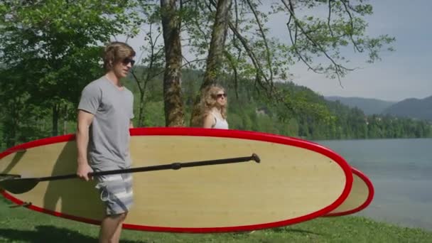 Slow motion närbild: ungt par redovisade stå upp paddelbrädor mot vatten — Stockvideo