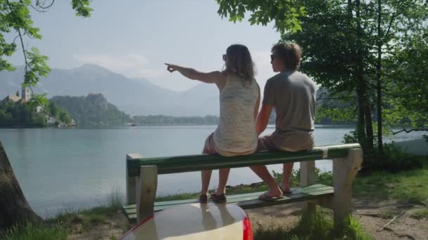 MOTION LENT : Petite amie et petit ami assis sur le banc au bord du lac avant SUPing — Video