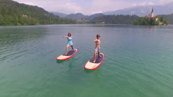 AERIAL: Flying around young couple doing yoga on SUP boards — Stock Video