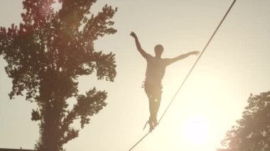 Yavaş Hareket: Yaz gün batımında yüksek slackline üzerinde yürüyen adam