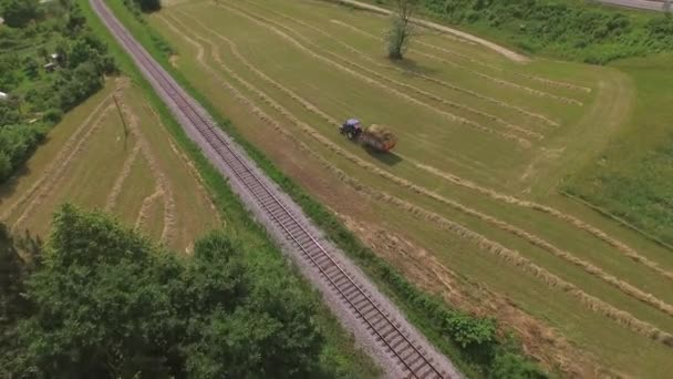 AERIAL: Фермер собирает сено с трактором на сельскохозяйственном поле — стоковое видео