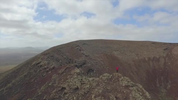 AERIAL: стоїть на краю вулканічного кратера з піднятими руками — стокове відео