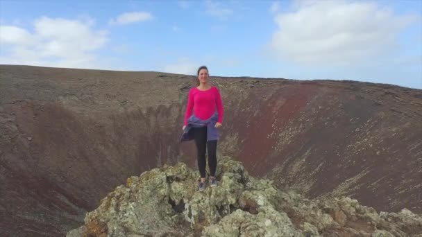 AERIAL: Happy female raising hands on top of volcanic crater — Stock Video