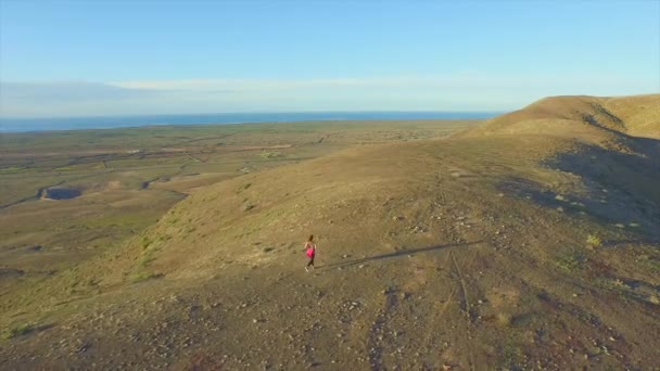 AERIAL: Женщина бегает на вершине вулкана в вулканическом ландшафте — стоковое видео