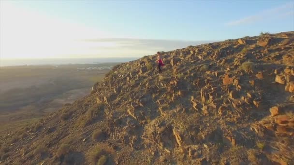 AERIAL: Mujer joven descendiendo por la montaña volcánica al atardecer — Vídeos de Stock