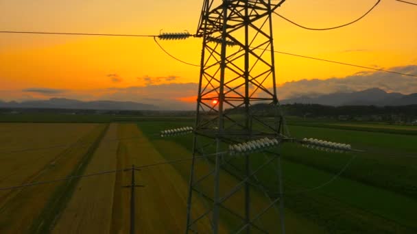 AERIAL: Voando até a torre de eletricidade de alta tensão ao pôr do sol — Vídeo de Stock