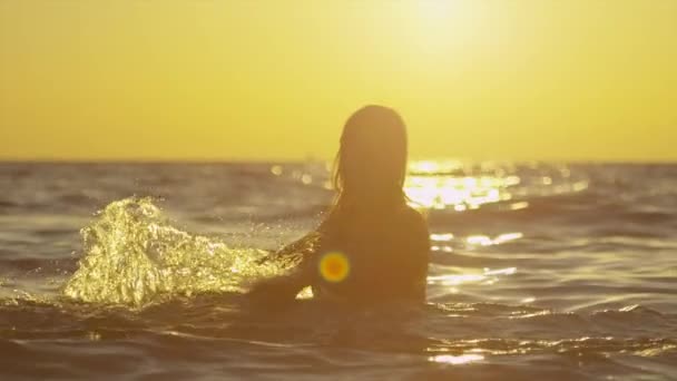 MOTION LENT : Heureuse femelle éclaboussant l'eau de l'océan au coucher du soleil doré — Video