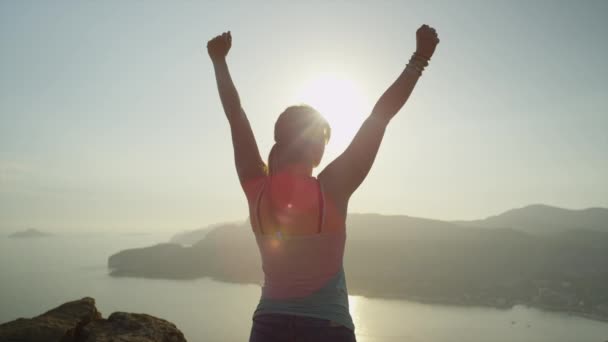 Mujer levantando brazos en la cima de la montaña sobre el cielo atardecer — Vídeos de Stock