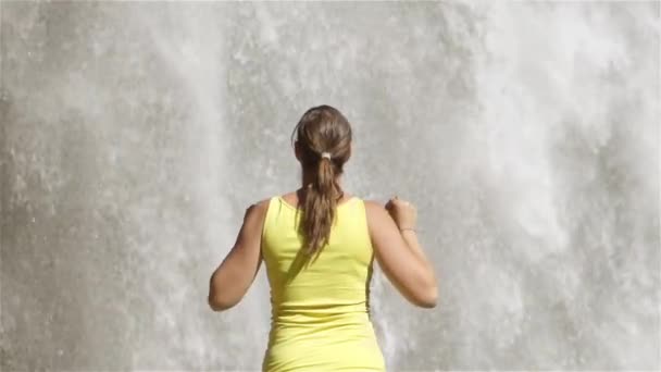 Медленное приближение: молодая женщина смотрит на водопад и празднует — стоковое видео
