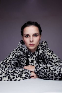 Kapüşonlu, açık renk arka planlı bir kadın.