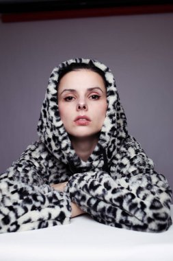 Kapüşonlu, açık renk arka planlı bir kadın.