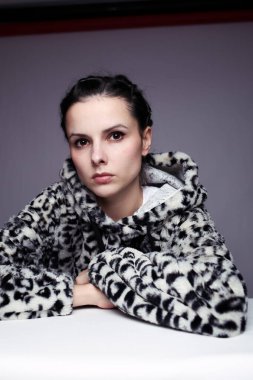 Kapüşonlu, açık renk arka planlı bir kadın.