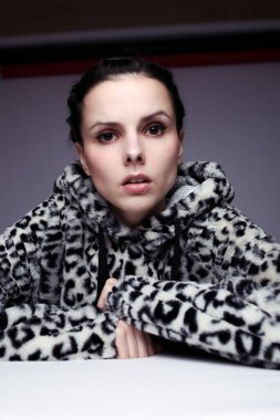 Kapüşonlu, açık renk arka planlı bir kadın.