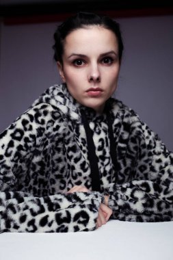 Kapüşonlu, açık renk arka planlı bir kadın.