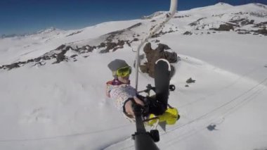 Snowboard 'cu dağda kayak asansörüne biner ve kamerada kendi fotoğrafını çeker.