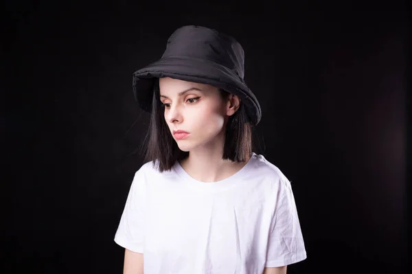 cute woman in white t-shirt and black panama hat, portrait on dark background